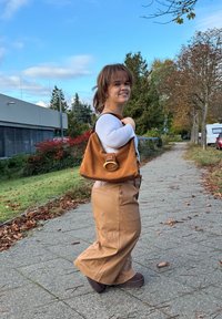 Tasche aus beigem Wildleder mit einer großen goldfarbenen Akzent-Hardware, kombiniert mit beigen, weit geschnittenen Hose aus Kunstleder und einem weißen Langarm-Oberteil.