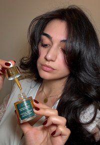 Donna che tiene in mano una bottiglia di olio per capelli e corpo Monpure shimmer and hydrate, utilizzando un contagocce per sollevare l'olio dorato dalla bottiglia.