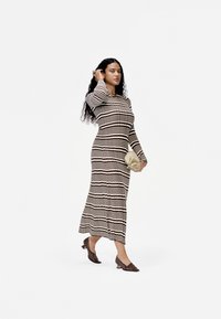 Vestido de malha de manga longa listrado em castanho e creme, com uma silhueta ajustada. Os acessórios incluem uma mala de mão de tom claro e sapatos com textura.