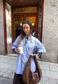 Light blue oversized button-up shirt, layered with a black-and-white patterned long sleeve top. Brown leather shoulder bag and a white coffee cup.