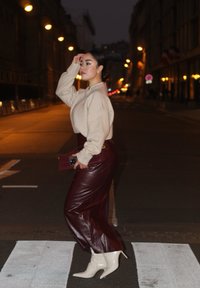 Beige stickad tröja, högmidjade vinröda faux läderbyxor och vita spetsiga ankelstövlar. Håller en röd kviltad clutch. Gata på natten.