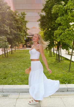 Conjunto blanco de dos piezas que incluye una blusa corta con tirantes y una falda maxi fluida, complementado con un bolso redondo de paja y sandalias de plataforma.