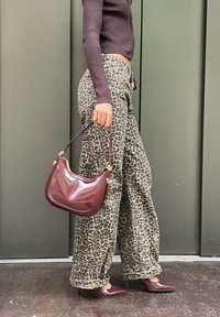 Lakovaná kožená kabelka farby burgundská červeň s oblým tvarom, zlatými kovovými doplnkami a širokými nohavicami s leopardím vzorom; modelka má na sebe špicaté burgundské lodičky.