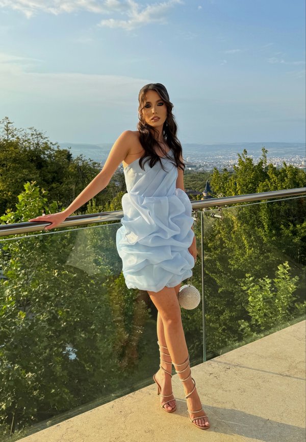 Light blue, strapless dress with layered ruffles. Accented with strappy heels and a round, silver clutch. Smooth fabric, knee-length cut.