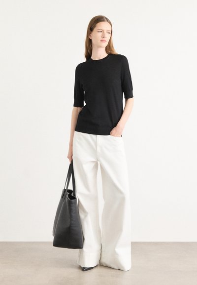 Top negro de manga corta combinado con pantalones anchos blancos. Lleva un gran bolso de piel negro y calza tacones negros de punta.