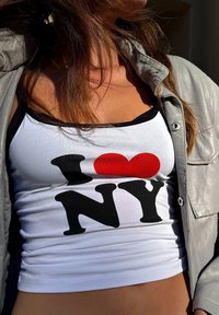 Vit linne med svart kant, med fet svart text "NY" och ett rött hjärta. Bärs under en ljusgrå skinnjacka.