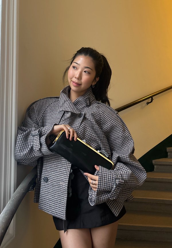 Grauer und weißer übergroßer Hahnentritt-Blazer mit großen Ärmeln, kombiniert mit einer schwarzen Clutch mit goldenem Akzent. Schlichte schwarze Shorts.