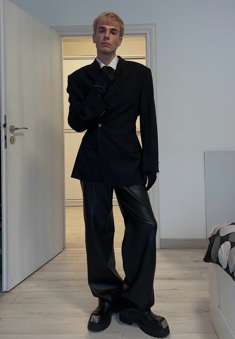 Blazer nero oversize con un bottone singolo e tasche, abbinato a pantaloni neri a gamba larga. Scarpe nere chunky e un guanto con trama.