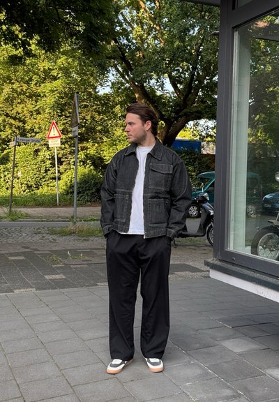 Chaqueta de mezclilla negra con cremallera frontal y bolsillos de parche, combinada con una camiseta blanca, pantalones negros y zapatillas multicolores.