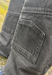 Črne denim cargo hlače z velikim stranskim žepom, strganim robom in vidnimi šivi. Teksturirano blago s klasičnim krojem.