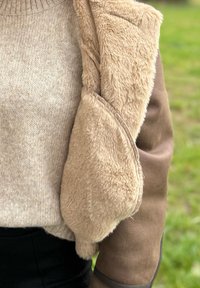 Beige striktrøje med ribbet halsudskæring, kombineret med en tanfarvet og fluffy fleecejakkeærme, der fremhæver tekstur og farvekontrast.