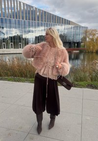 Faux fur pink jakke, lagdelt blonde top, sorte bukser med bred ben, og grå knæhøje støvler. Mørk håndtaske med et stilrent design.