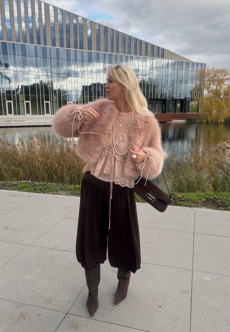 Faux fur pink jacket, layered lace top, black wide-leg trousers, and gray knee-high boots. Dark handbag with a sleek design.