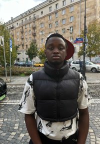 Czarna kamizelka puffer na białej koszuli w czarne nadruki koni. W tle widać miejskie budynki i zaparkowane samochody.