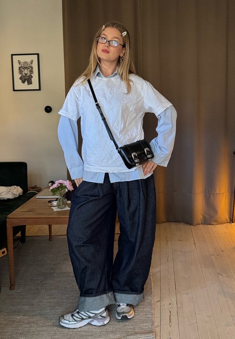 Överdimensionerad vit och ljusblå skjorta i lager med vida jeansbyxor. Tillbehör inkluderar svart crossbody-väska och sneakers.