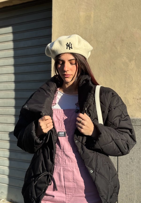 Chaqueta acolchada negra, peto rosa con etiqueta Vans, camiseta blanca y boina crema con logo de NY. Texturas suaves y diseño en capas.
