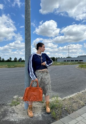 Navy-blaues Sportoberteil mit weißen Streifen, kombiniert mit leopardmusterte Culottes. Eine orangefarbene Handtasche und beigere Stiefel runden das Outfit ab.