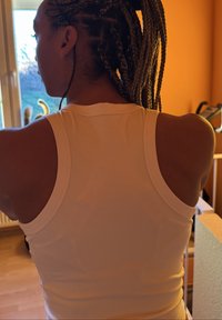 Débardeur blanc sans manches avec un col arrondi et une texture lisse, vu de dos, mettant en valeur la forme des épaules et des bras.