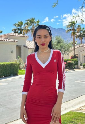 Rød tætsiddende kjole med lange ærmer, hvid V-udskæring og tre hvide striber ned ad hver ærme. Har et lille logo på brystet.