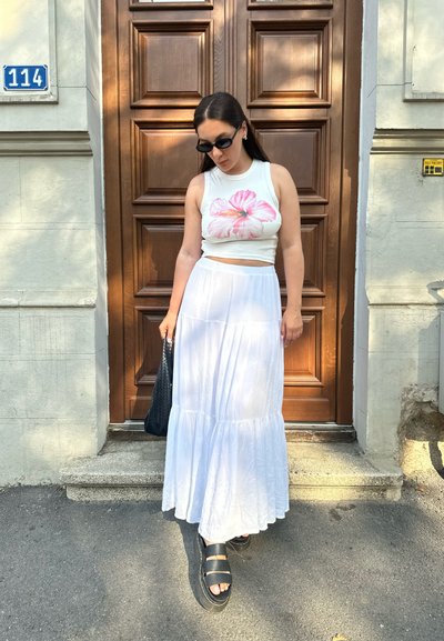 Top corto blanco con estampado floral rosa, falda maxi blanca en capas y sandalias de plataforma negras. Un bolso de mano tejido en negro completa el conjunto.