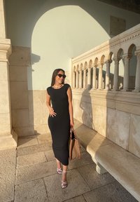 Μαύρο εφαρμοστό φόρεμα με κοντά μανίκια, συνδυασμένο με λευκές λουράτες γόβες και μια τσάντα από πλέξη σε καφέ χρώμα. Λείο ύφασμα, κομψή σιλουέτα.