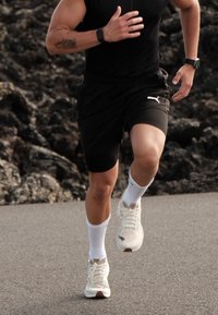 Zwarte sportshorts, witte sokken en lichte sneakers met tan accenten. Persoon die rent op een gestructureerd, donker oppervlak.