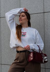 Λευκό cropped φούτερ με γραφικό τύπωμα, καφέ παντελόνι σε ψηλή μέση, μαύρη ζώνη και μπορντό τσάντα χειρός με αλυσιδίτσα. Λείος υφασμάτινος τύπος.