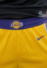 Gele basketbalschoenen met een paarse tailleband die het "Los Angeles Lakers"-logo en een klein blauw Nike-swoosh aan de zijkant heeft.