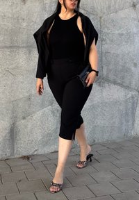 Crna majica bez rukava u kombinaciji s crnim zakrpama hlačama sa otvorima. Dodaci uključuju crnu torbicu i sandale s potpeticama u leopardskom uzorku.