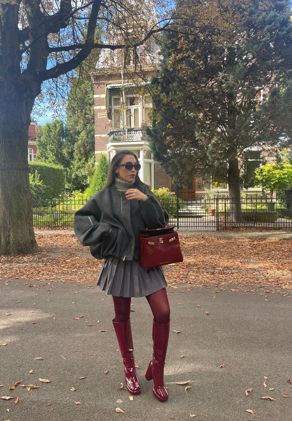 Γκρίζα υπερμεγέθη ζακέτα, πλισέ γκρίζα φούστα, μπορντό μπότες μέχρι το μηρό και μια τσάντα που ταιριάζει. Μαύρα γυαλιά ηλίου συμπληρ�ώνουν το ντύσιμο.