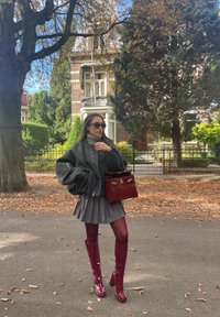 Γκρίζα υπερμεγέθη ζακέτα, πλισέ γκρίζα φούστα, μπορντό μπότες μέχρι το μηρό και μια τσάντα που ταιριάζει. Μαύρα γυαλιά ηλίου συμπληρώνουν το ντύσιμο.