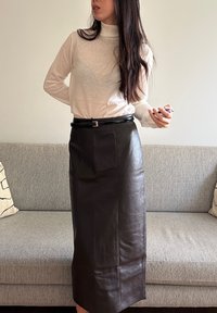 Černá kožená sukně se rovnou siluetou, do kolen, s přední kapsou a úzkým černým páskem. Stylová s svetrem se stojáčkem v světlé barvě.