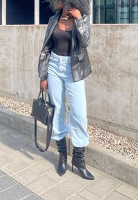 Čierny kožený blejzer cez čierny bodysuit, svetlomodré džínsy s vysokým pásom, čierne voľné kotníkové topánky a malá čierna kabelka.