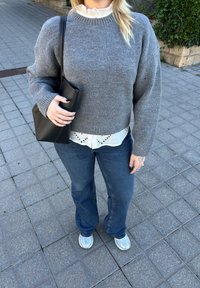 Grå strikkegenser, hvit skjorte med volanger og hullbroderi, blå vide jeans og sølvfargede joggesko. Svart veske holdt i den ene hånden.