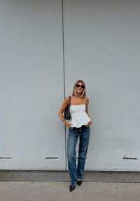 Top peplum branco com alças finas, combinado com jeans de ganga azuis. Acessórios incluem uma mala preta e sapatos de salto agudo pretos.