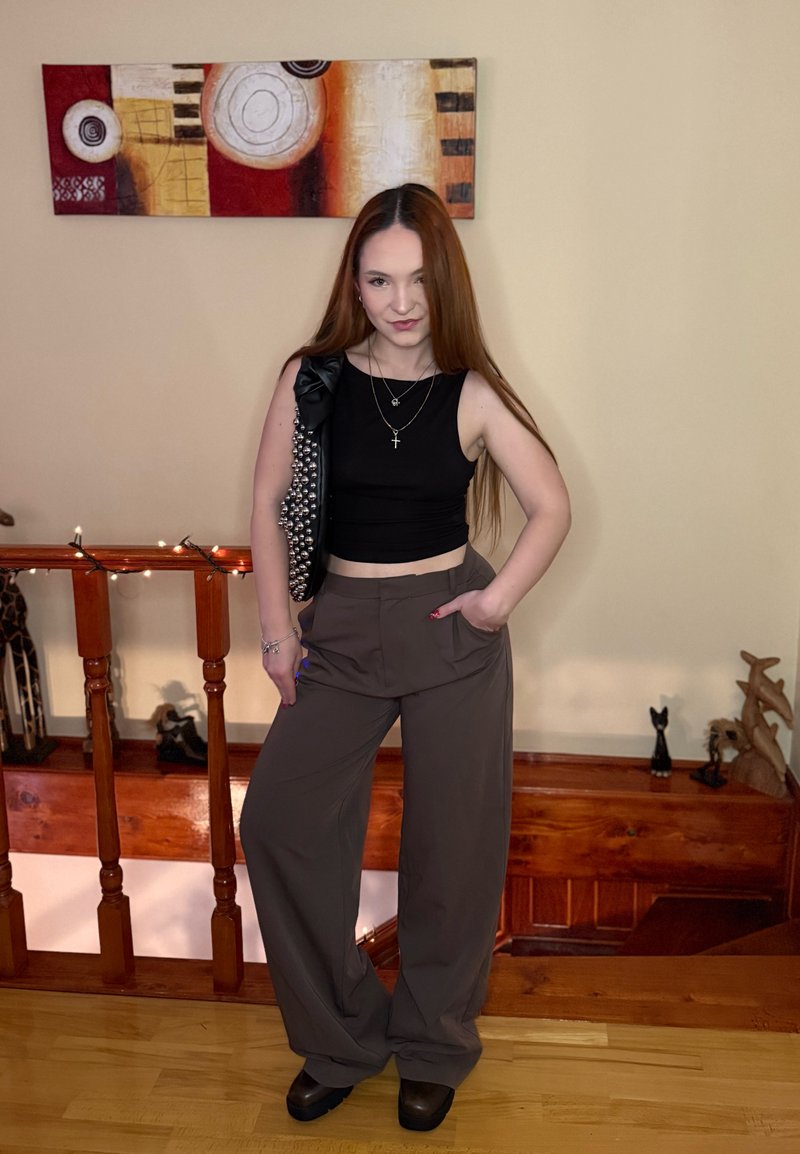Débardeur noir court et pantalon marron à jambes larges. Accessoires comprenant des colliers superposés et un gilet noir orné avec un nœud.