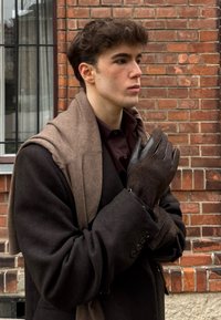 Brun uldfrakke med et kontrasterende brunt tørklæde, holder brune og sorte handsker. Tekstureret brunt stof står i kontrast til glatte læderdetaljer.