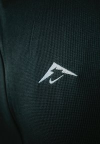 Črn teksturiran material s majhnim belim vezem logotipom, ki spominja na strelo, je nameščen v spodnjem desnem kotu.