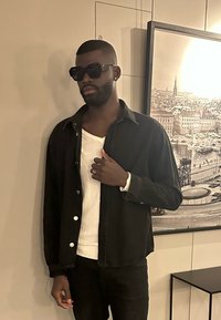 Czarna kurtka dżinsowa noszona na białym swetrze, z luźnym krojem i guzikami. Do zestawu dołączone ciemne okulary przeciwsłoneczne i srebrny pierścionek.