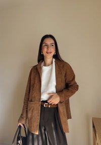 Brūns zamša žakete ar apkakli, divas priekšējās kabatas, komplektā ar baltu sporta kreklu un tumšām biksēm. Aprīkots ar brūnu jostu un rokassomu.