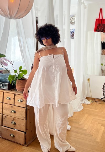 Top sin mangas ligero y blanco con cuello ajustable, combinado con pantalones blancos holgados. Textura suave, ajuste relajado y diseño minimalista.