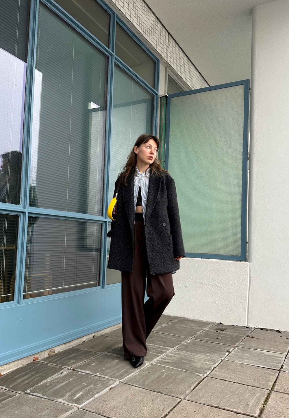 Μαύρο παλτό από μαλλί με υφή, γκρι ριγέ μπλούζα και καφέ φαρδύ παντελόνι. Κίτρινη τσάντα ως ένδειξη αντίθεσης; σύγχρονος, μινιμαλιστικός σχεδια σμός.