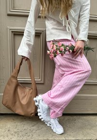 Pantalones de pierna ancha a rayas rosas, blusa blanca texturizada, bolso de hombro de cuero marrón, zapatillas blancas con amortiguación distintiva y flores rosas.