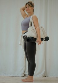 Crop top court en lavande pâle côtelé, leggings noirs taille haute, et un grand sac beige tenant un tapis de yoga noir, sur un fond neutre.