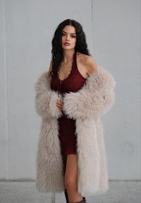 Umelá kožušina v svetlej béžovej s nadrozmernými rukávmi, nosená cez bordové šaty s viazaním vpredu a textúrovanou l�átkou.