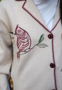 Beež kardigan, millel on detailne marooni- ja rohelise värvi tikandiga öökulli muster, maroonid nööbid ja kontrastõmblused servadel.