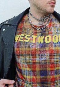 T-skjorte med flerfarget rutemønster i rødt, gult og blått, med "WESTWOOD" i fete gule bokstaver. Brukt under en svart skinnjakke.