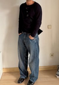 Mustad pikkade varrukatega must särk nupuga detailiga, koos helesiniste denim teksadega. Õhuke must kott kantud üle keha, jalanõud on mustast nahast.