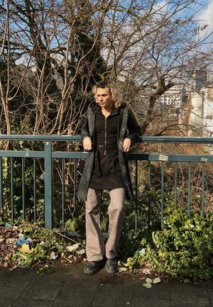 Chaqueta negra con cremallera y capucha, cinturilla ceñida sobre vestido oscuro, combinada con pantalones de leopardo de pierna ancha y zapatos negros gruesos.