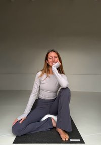 Haut à manches longues gris clair associé à un pantalon évasé gris foncé, assis sur un tapis de yoga noir, avec un fond uni.